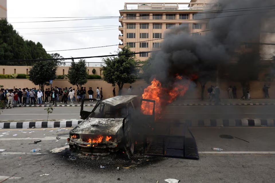 Orang-orang berdiri di dekat sebuah kendaraan yang dibakar oleh para demonstran saat aksi protes menentang korupsi dan keputusan pemerintah memblokir sejumlah platform media sosial, di Kathmandu, Nepal, 8 September. Sumber foto : REUTERS
